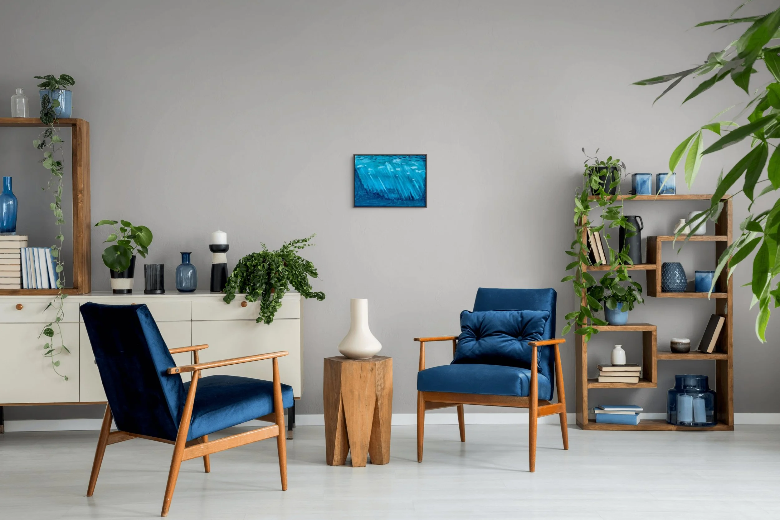 Living room with blue velvet chairs, wooden furniture, and shelves with blue vases and plants against a white wall.