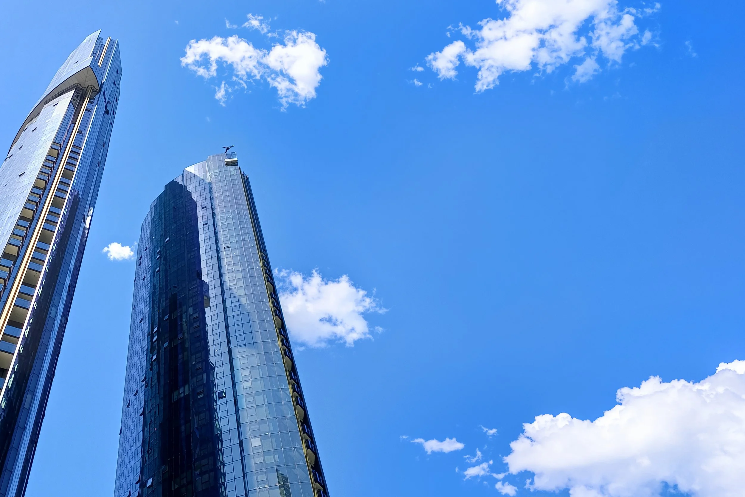 A photo of two tall, modern skyscrapers with reflective glass windows against a bright blue sky with some white clouds.