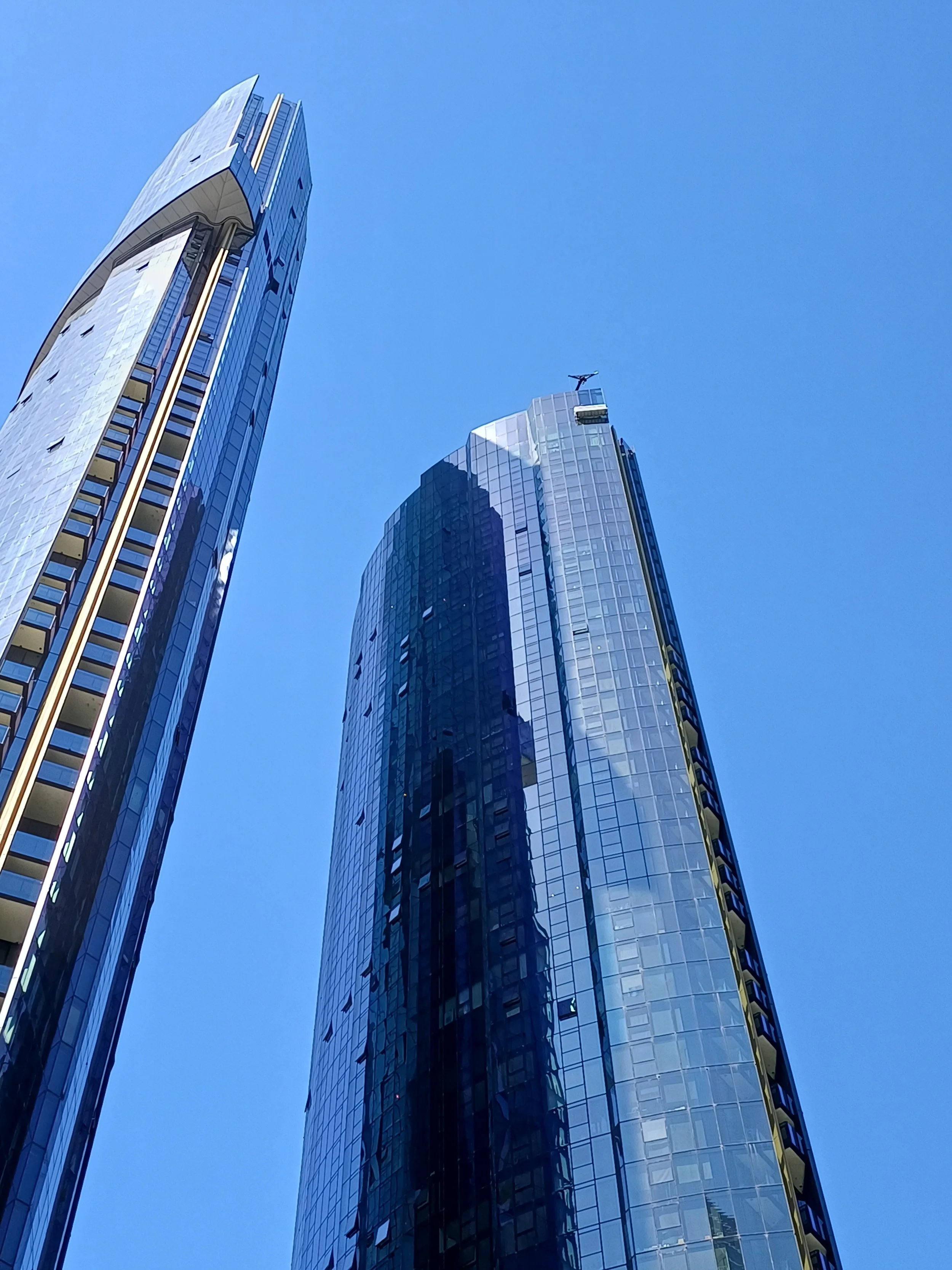 Three modern glass skyscrapers under a clear blue sky, with one building having an antenna on top.