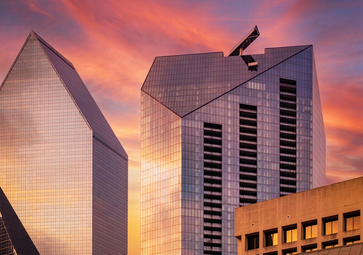 Modern glass skyscrapers reflecting a sunset sky with pink, orange, and purple hues.