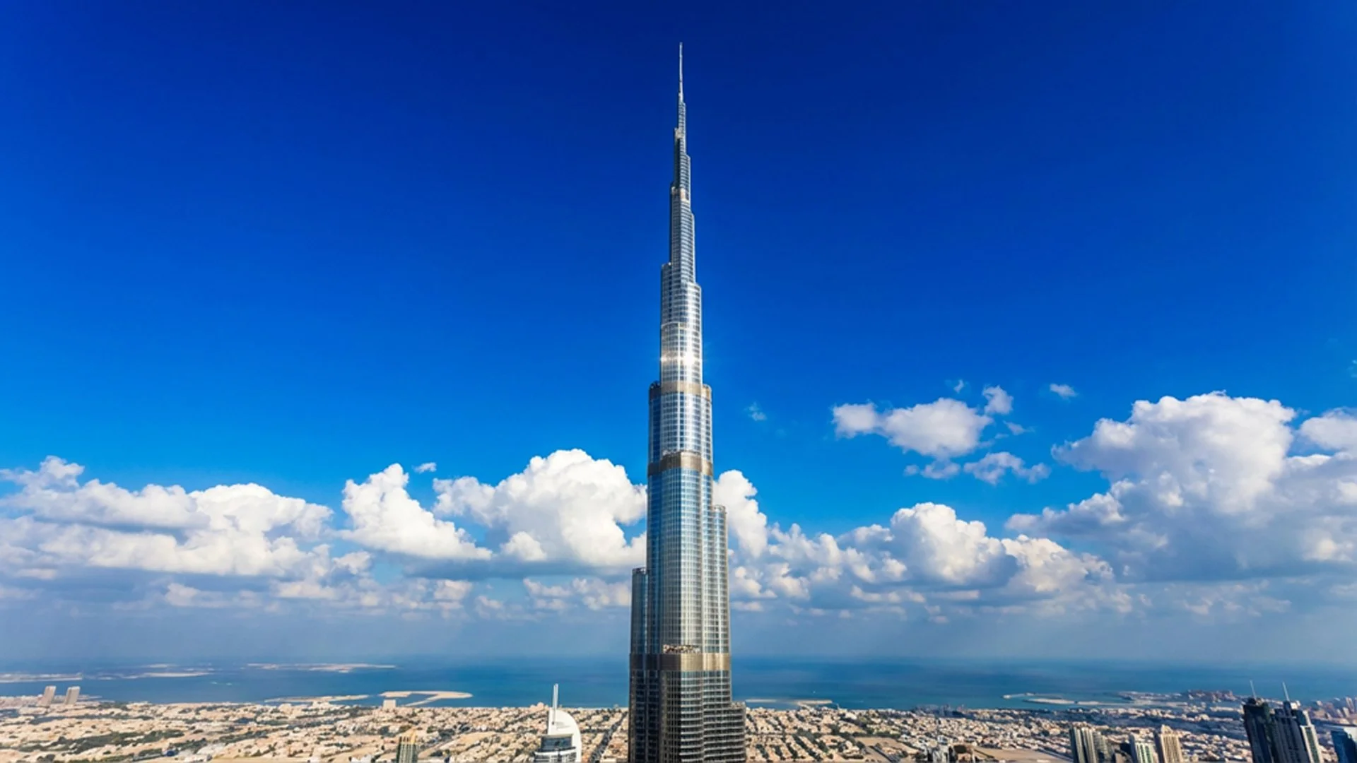 Tall skyscraper, Burj Khalifa, under a partly cloudy blue sky, overlooking the cityscape of Dubai.