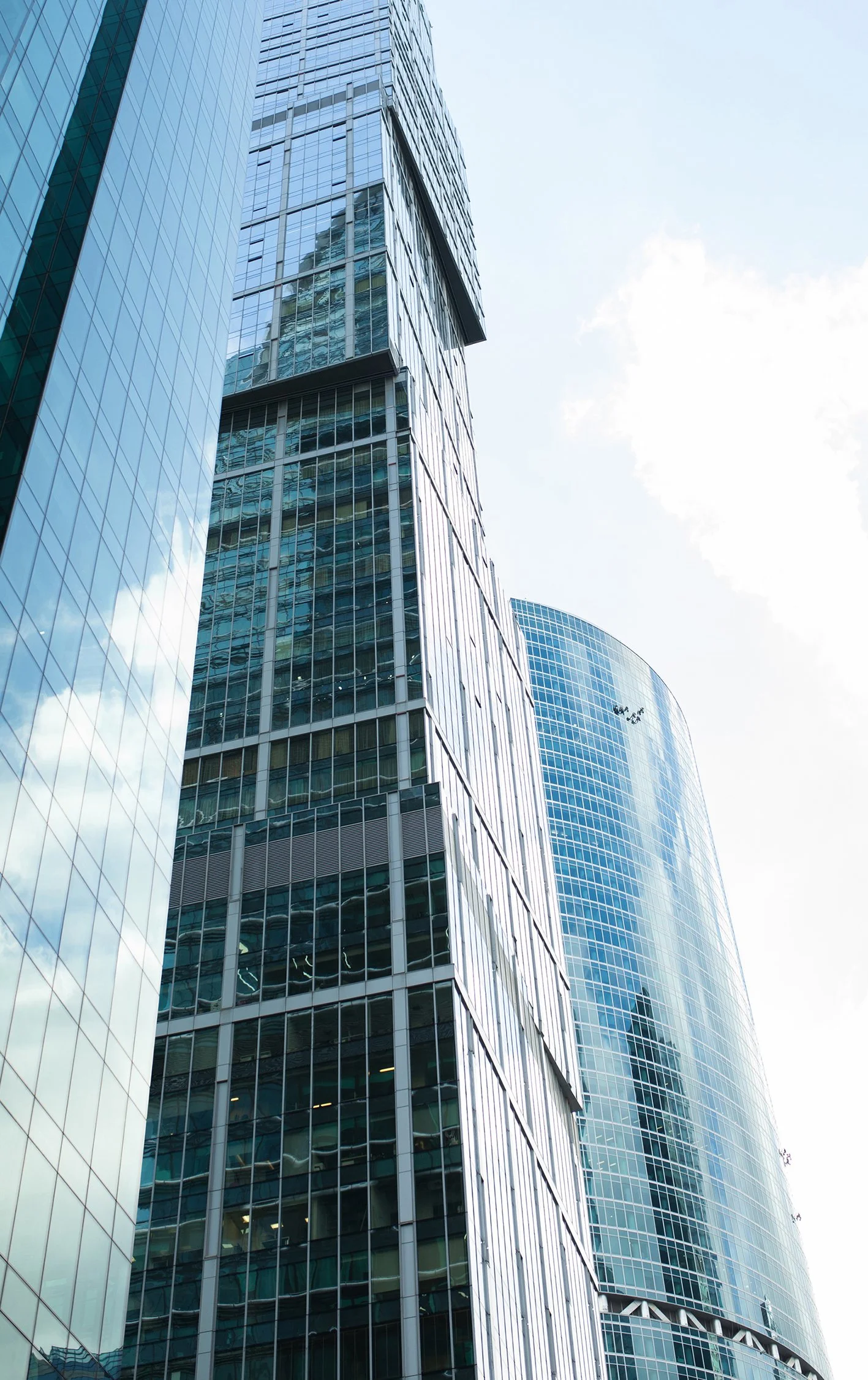Multiple modern glass skyscrapers reflecting the sky, with a clear sunny sky in the background.