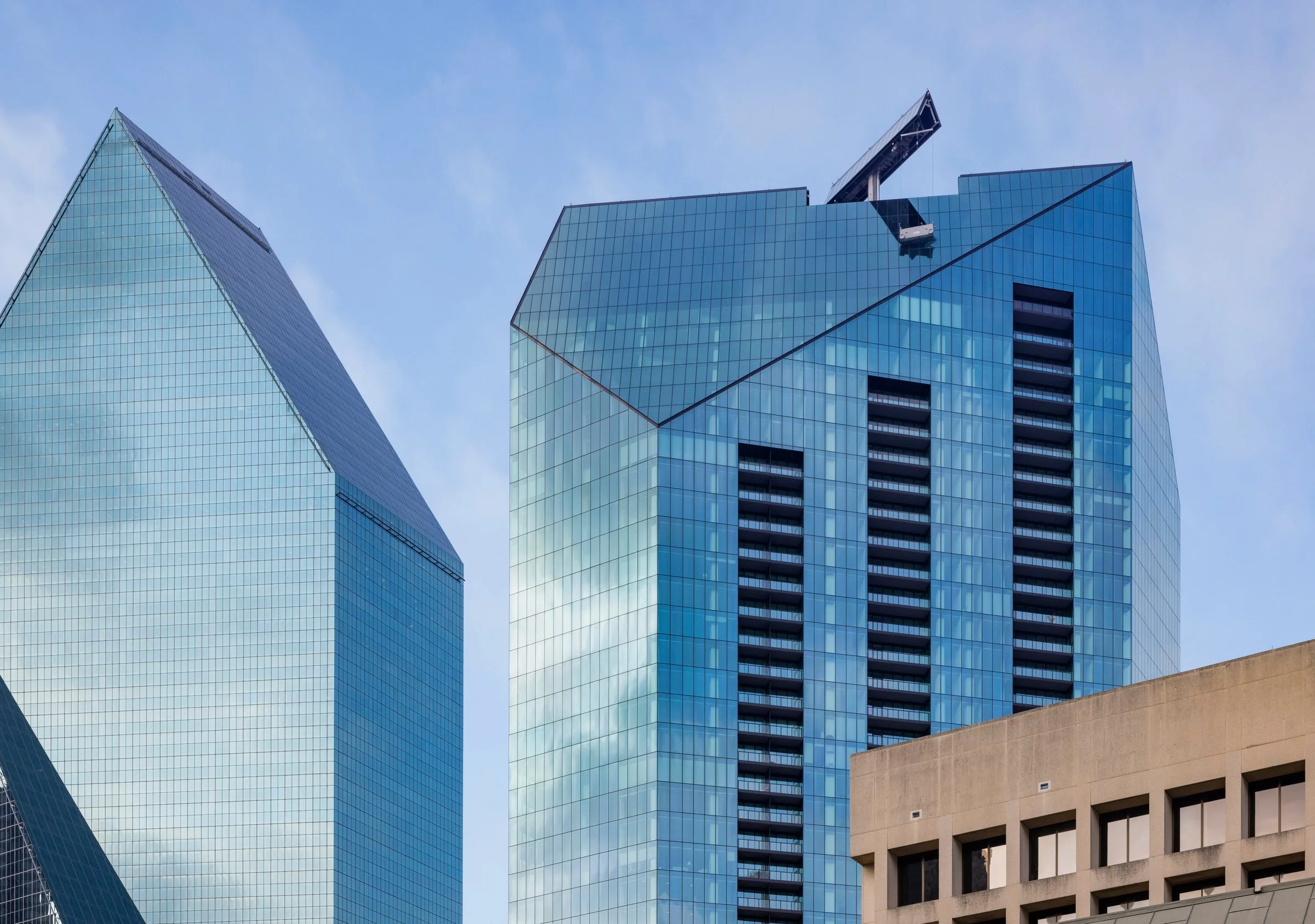 Three modern glass skyscrapers with reflective windows under a cloudy blue sky, with a concrete building at the bottom.