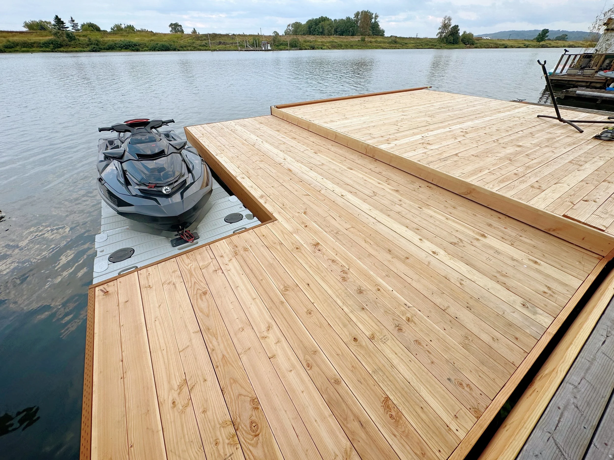A wooden dock on a body of water with an all-terrain vehicle and a scooter parked on it, and some trees in the background.