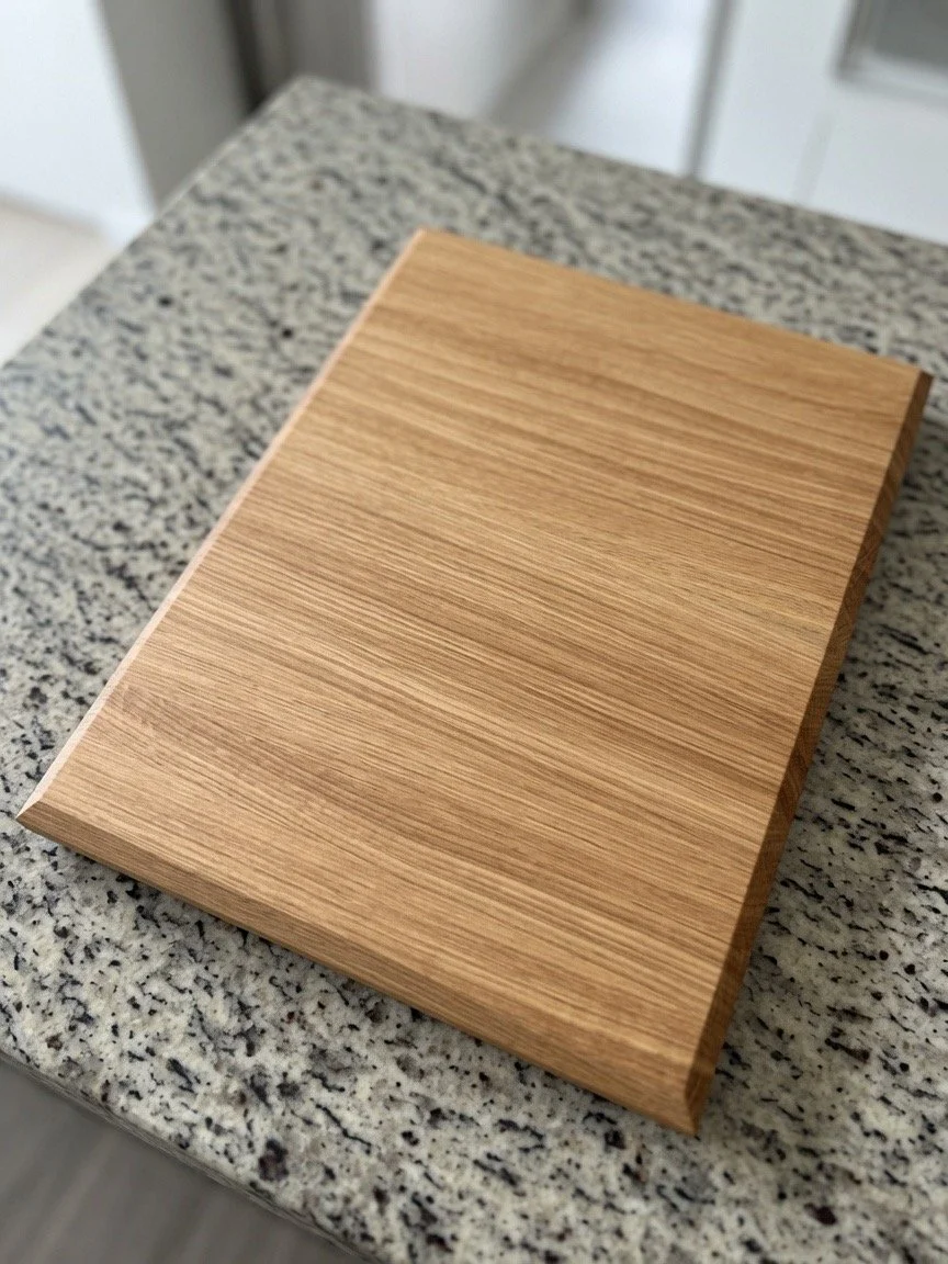 A rectangular wooden cutting board with rounded edges on a speckled gray and white granite countertop.