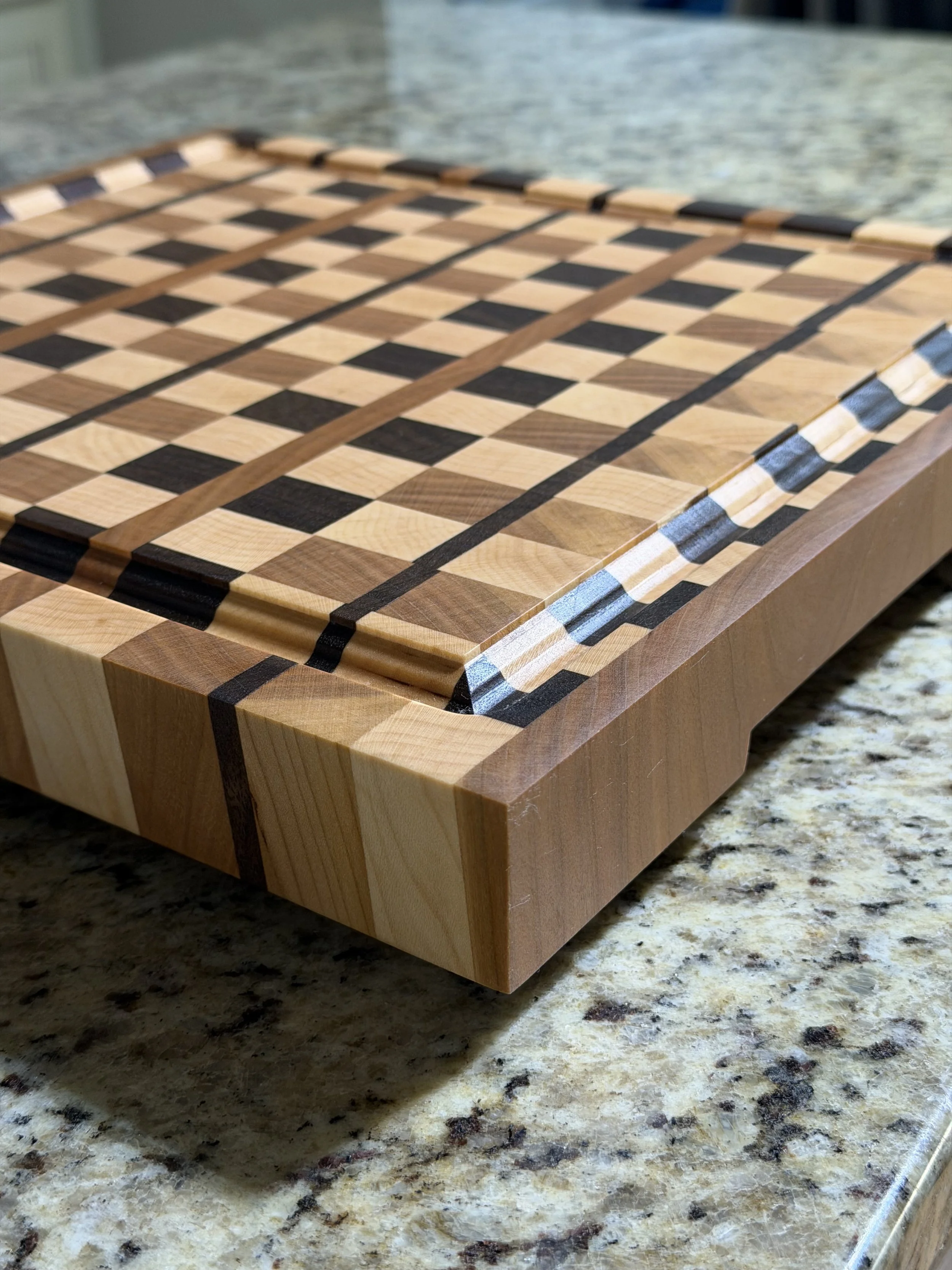 A wooden chessboard with alternating light and dark squares, placed on a granite countertop.