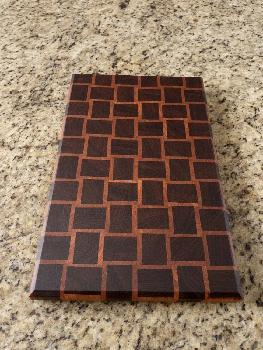 A rectangular wooden object with a checkered pattern of dark and light wood squares on a granite countertop.