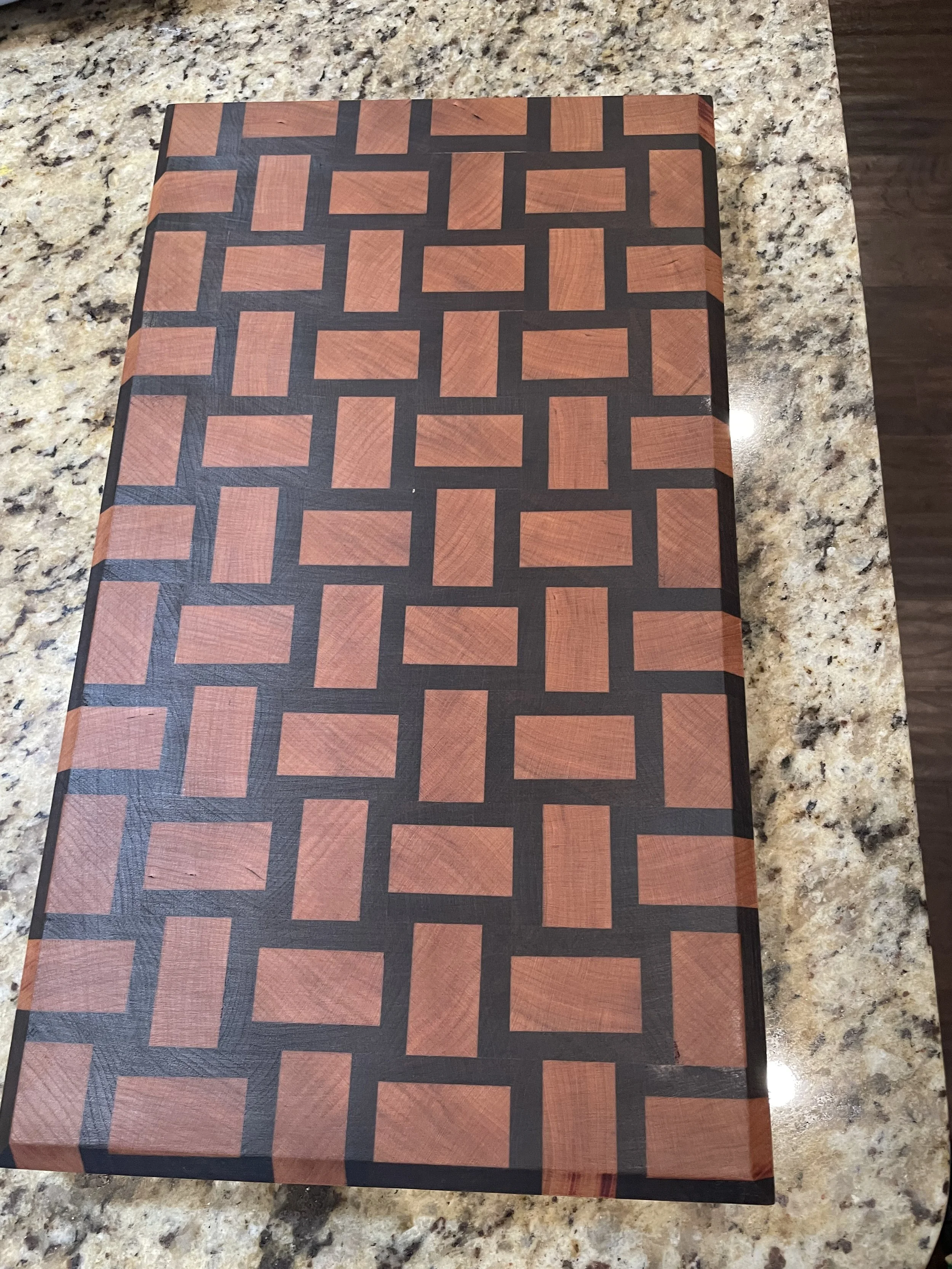 A rectangular box with a geometric pattern of red and black squares and rectangles on its lid, placed on a speckled beige and brown granite countertop.