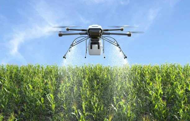 A drone spraying pesticides over a green crop field under a blue sky.
