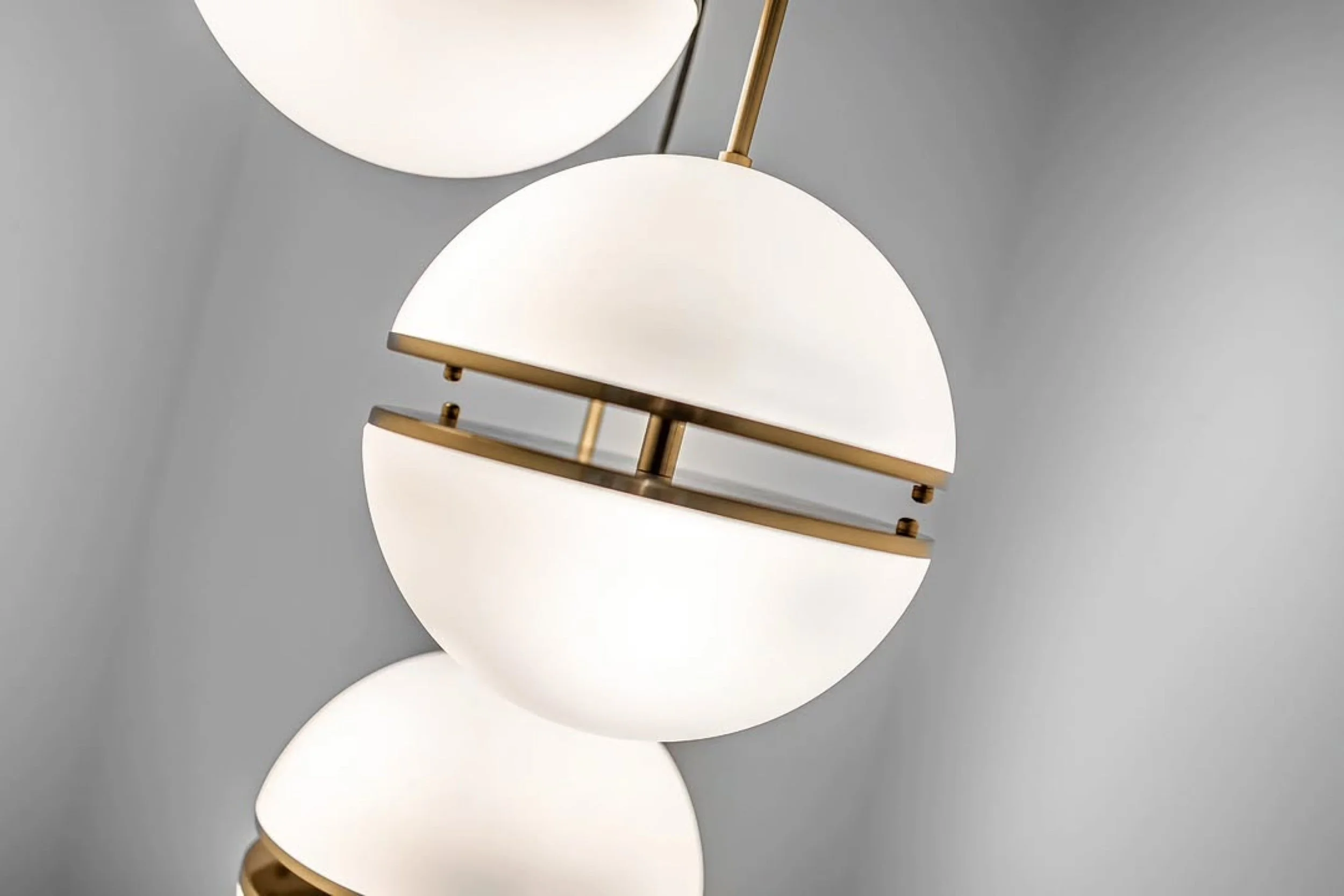 Modern hanging light fixture with white globes and gold accents against a gray wall.
