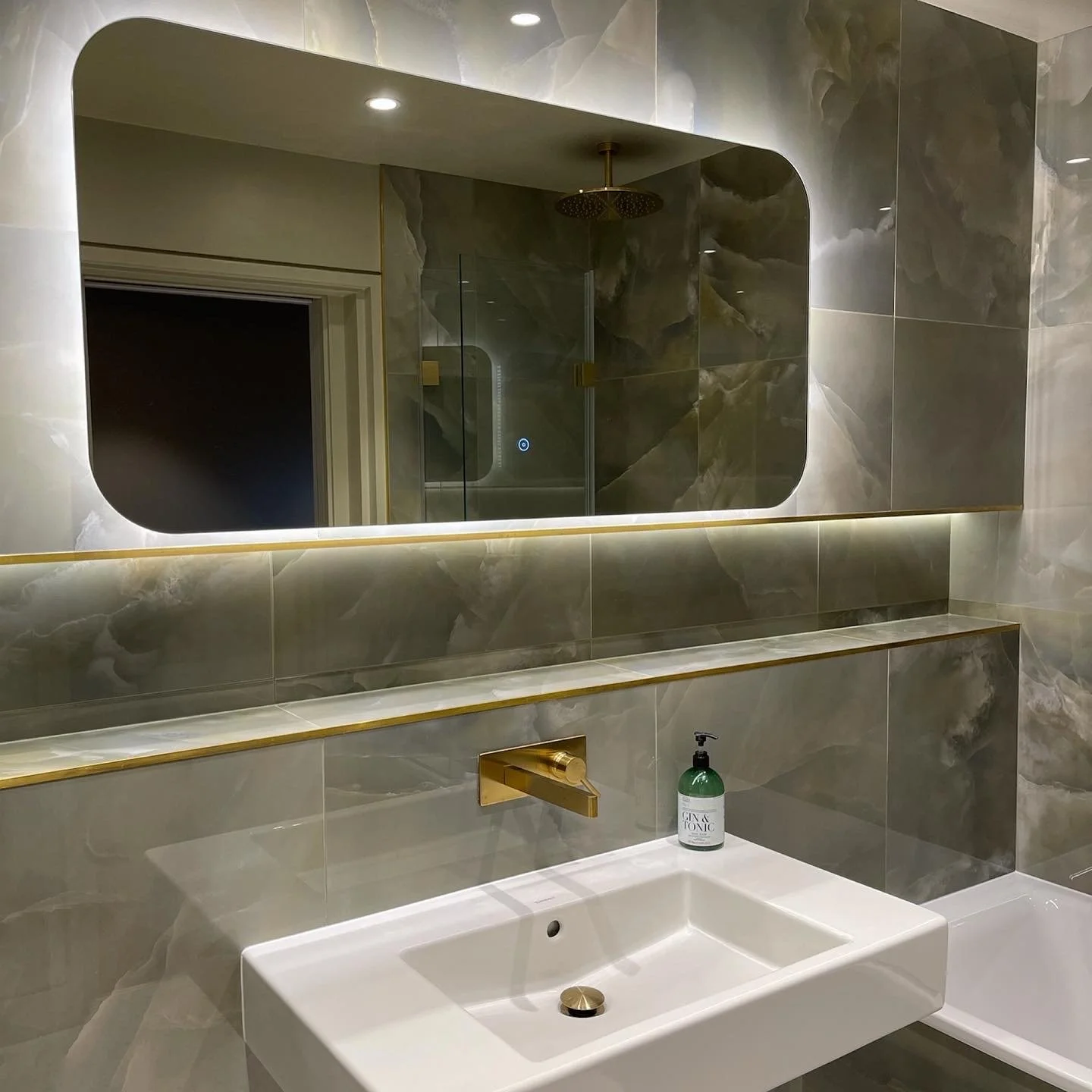 Modern bathroom with marble walls, large mirror, gold fixtures, and a white rectangular sink.
