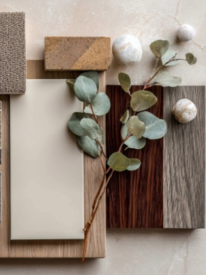 Flat lay of various material swatches, a eucalyptus branch, and decorative spheres on a neutral background.