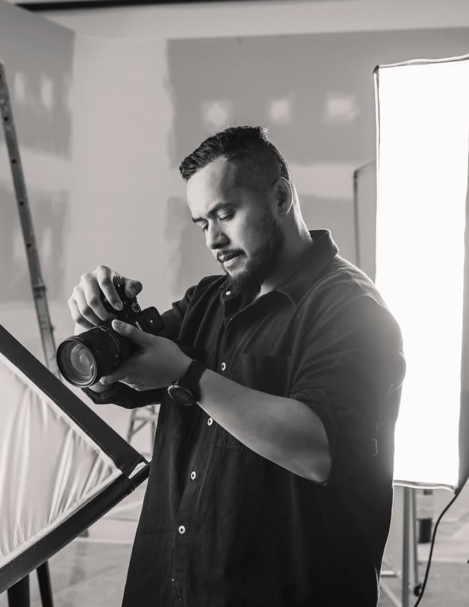 Man with dark hair and beard adjusting camera in photography studio with lighting equipment.