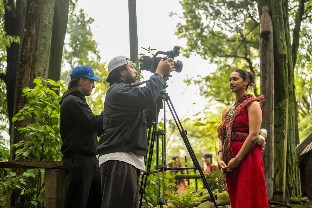 Filmmakers recording a woman in a red dress in a lush, green outdoor setting.