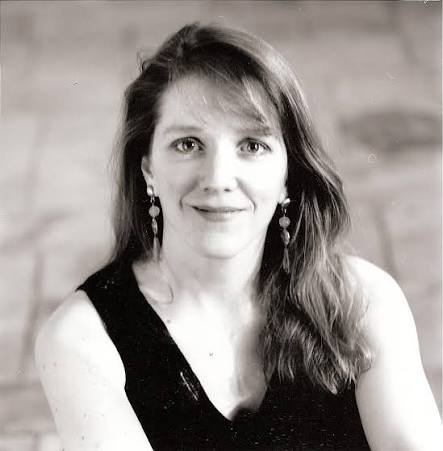 Black and white portrait of soprano Emily Van Evera with long hair, wearing earrings and a sleeveless top, smiling at the camera.