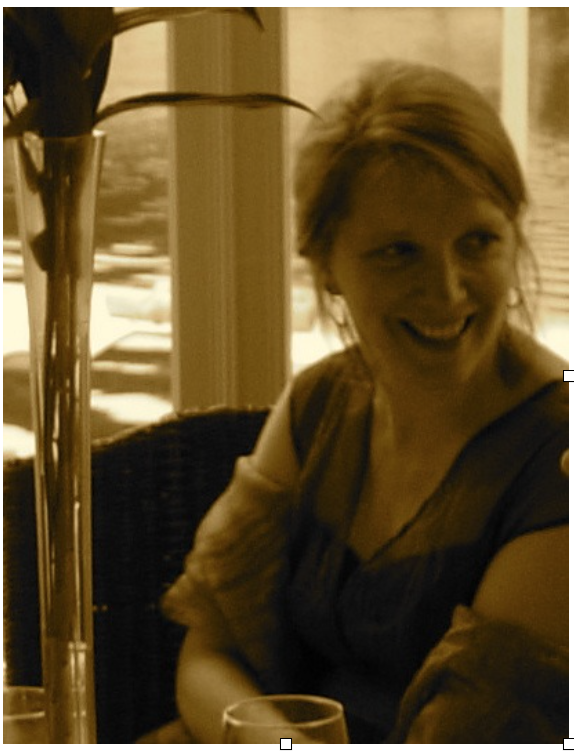 Emily Van Evera sits with smiling at a restaurant table near a window with a plant nearby.