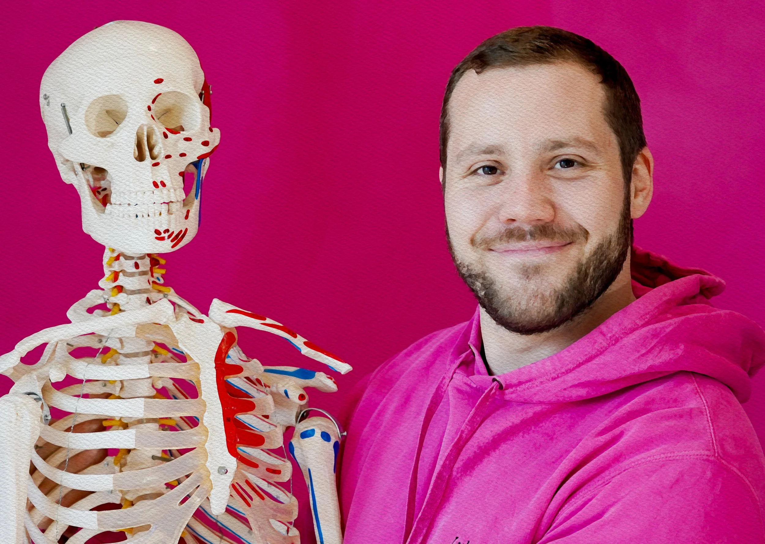 Ein Mann mit braunen Haaren und Bart trägt ein pinkfarbenes Sweatshirt, steht vor einem rosa Hintergrund, neben einem menschlichen Skelettmodell.