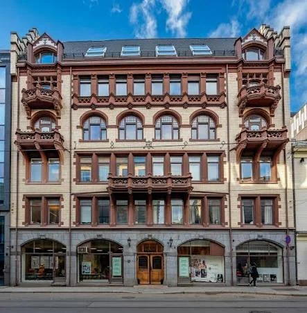 Bygning med flere etasjer og ornamentert fasade, med butikker i første etasje og klinikker i etasjene over.