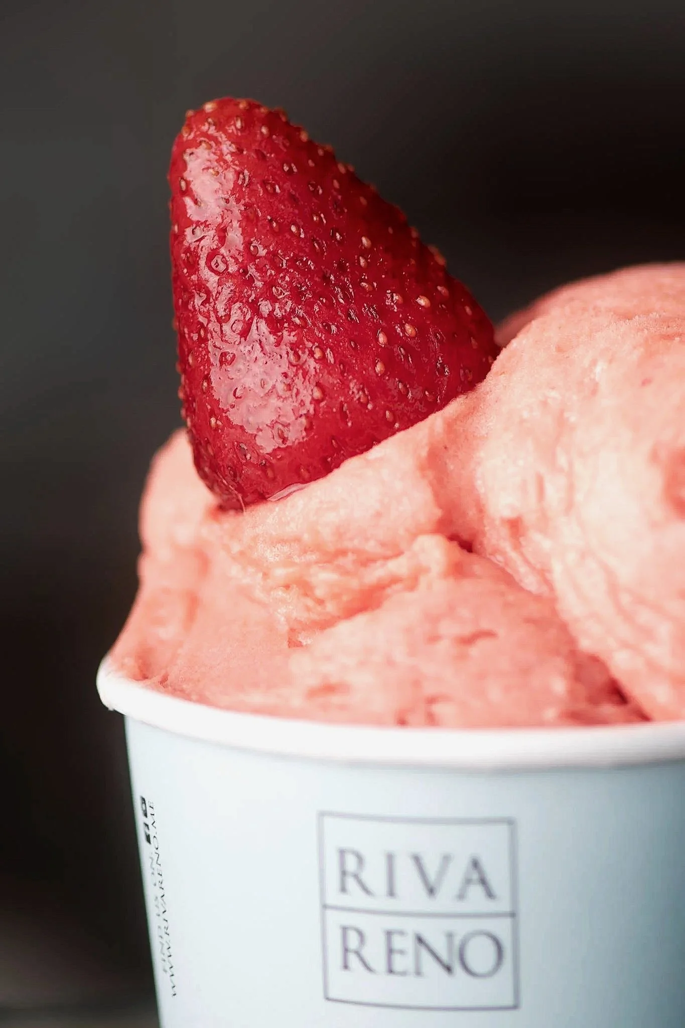 Close-up of strawberry ice cream in a cup with a frozen strawberry on top.