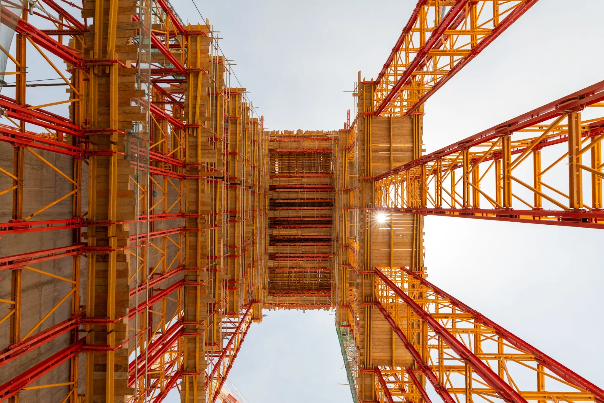 Construction site with orange and yellow scaffolding and framework for a building under construction, shot from below against a clear sky.