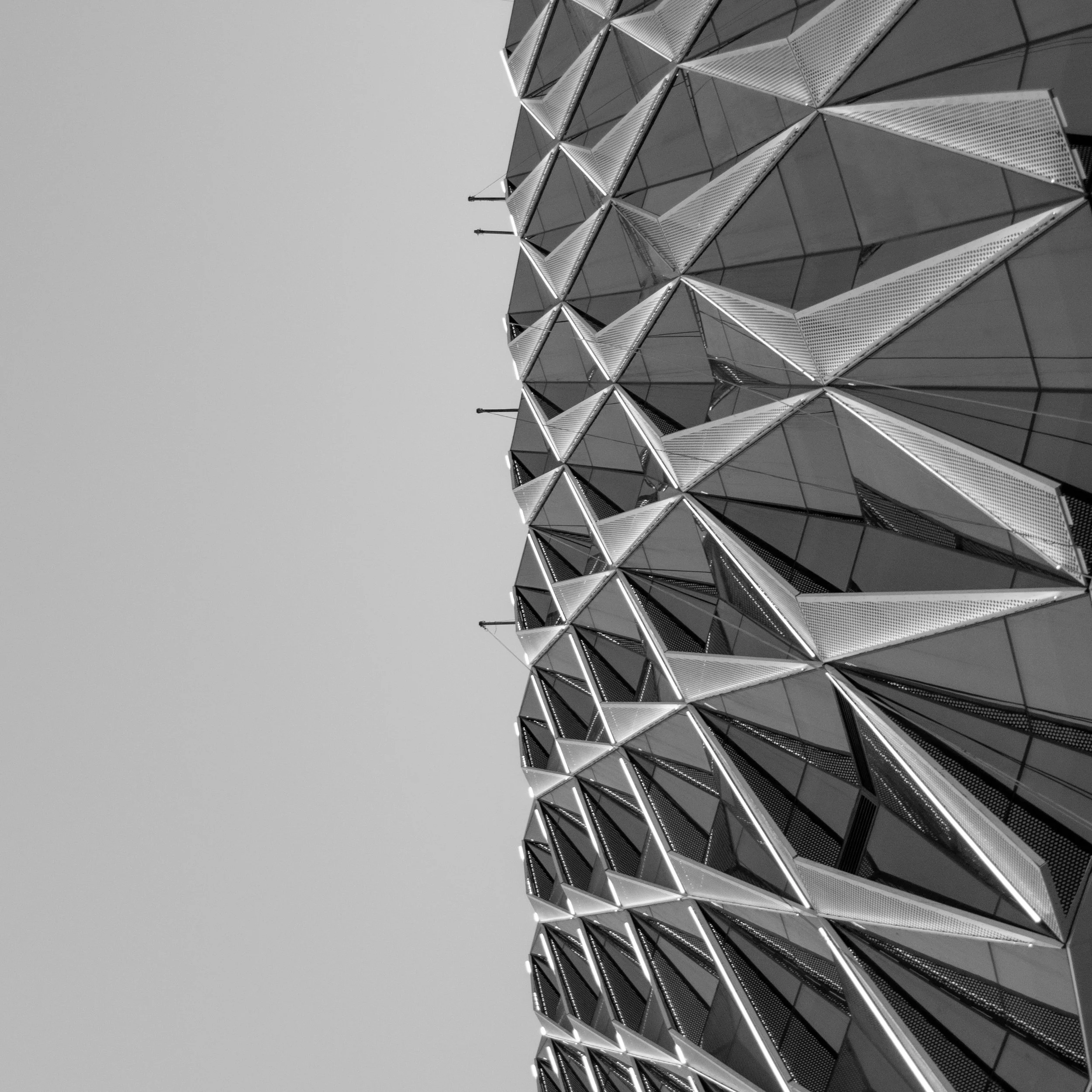 Close-up view of a modern building with a geometric, patterned facade made of reflective metal panels, viewed from below against an overcast sky.