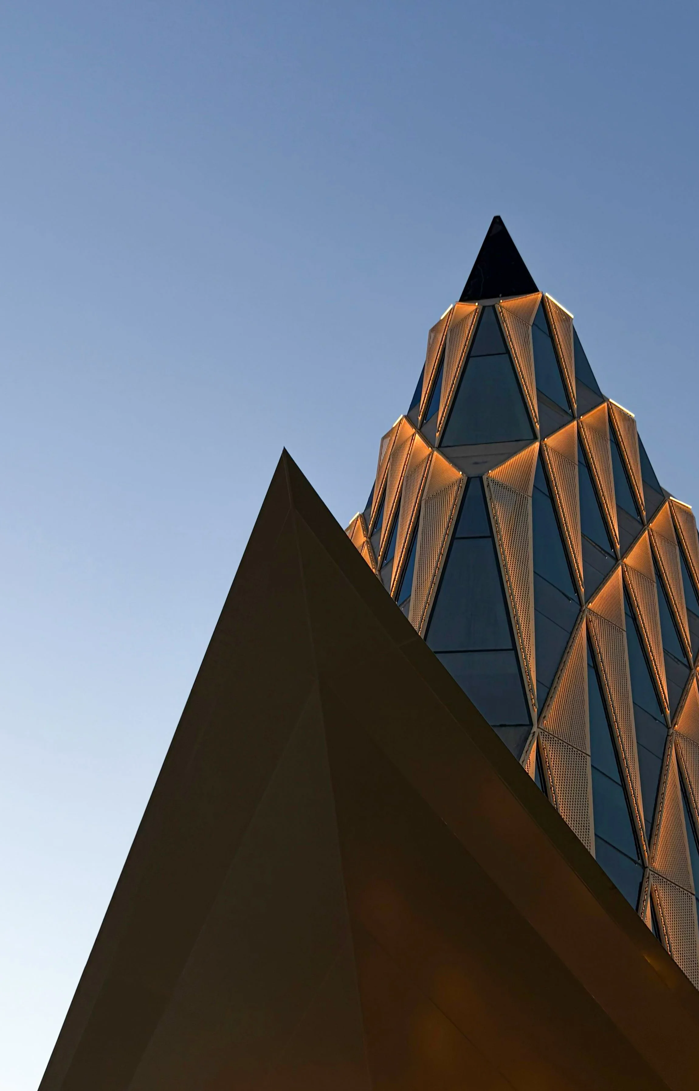 View of a modern building with geometric design and illuminated edges against a clear evening sky.