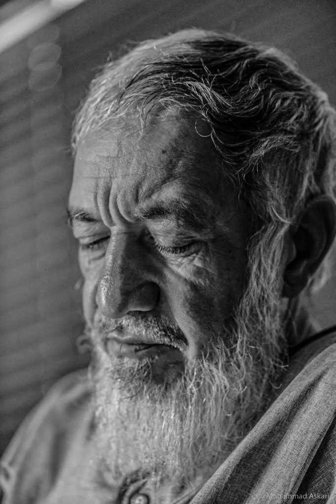 Close-up black and white portrait of an elderly man with a beard and mustache, eyes closed, with detailed facial features and hair.