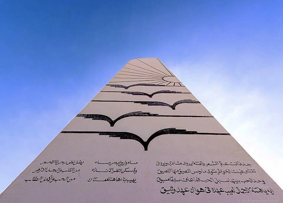 A tall, upward-looking view of a wall with black bat symbols and Arabic text.