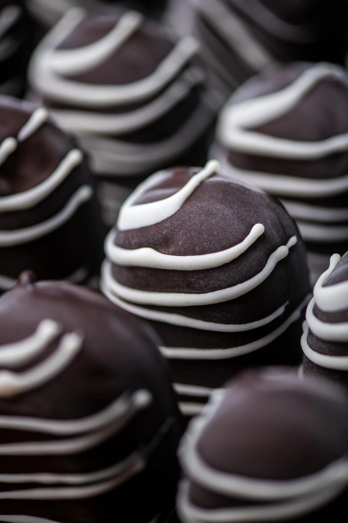 Close-up of numerous chocolate cookies decorated with white icing drizzle.