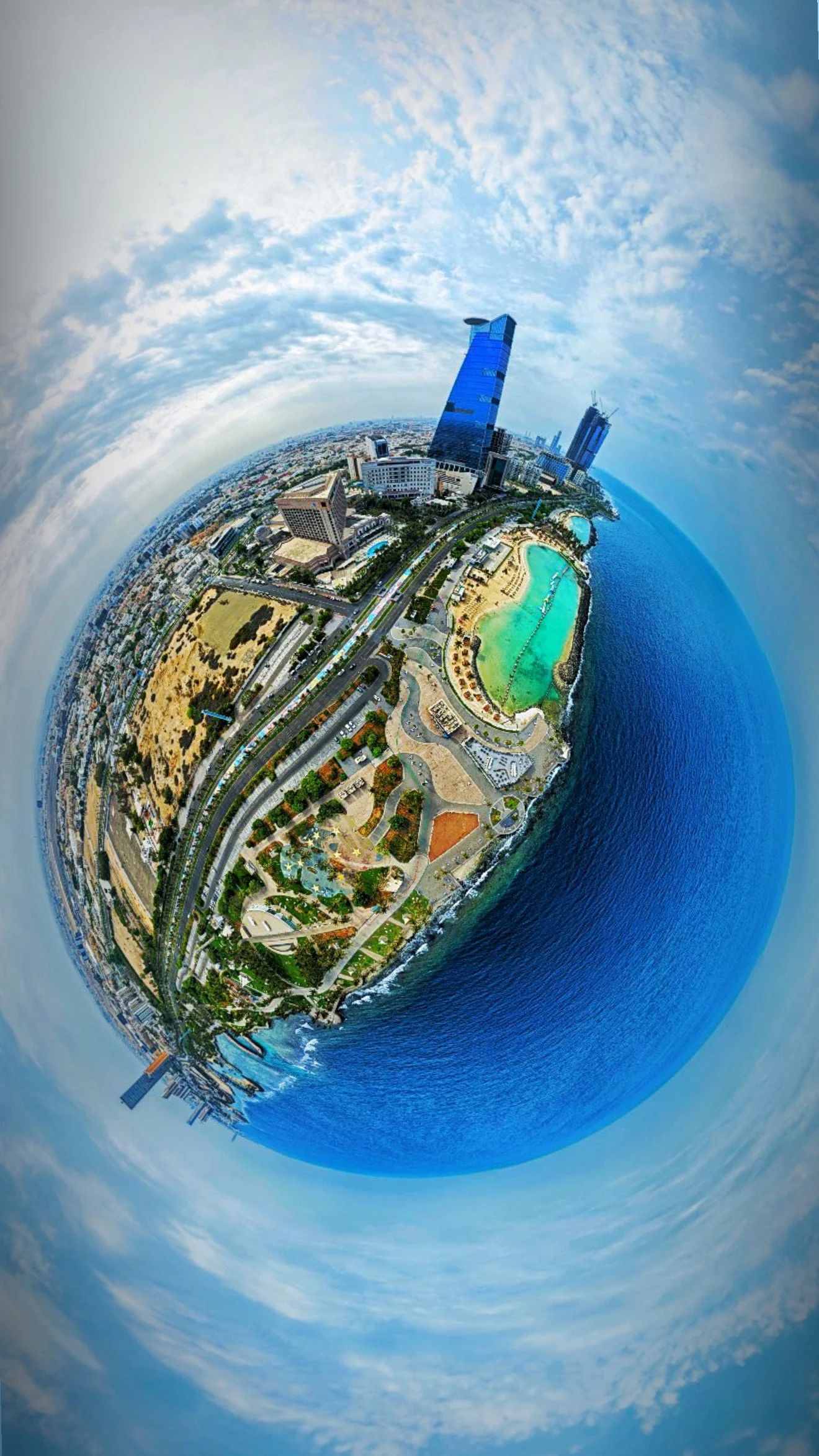 Panoramic aerial view of a city along the coast with a beach, tall buildings, roads, and green parks, taken with a fisheye lens creating a circular, distorted effect.