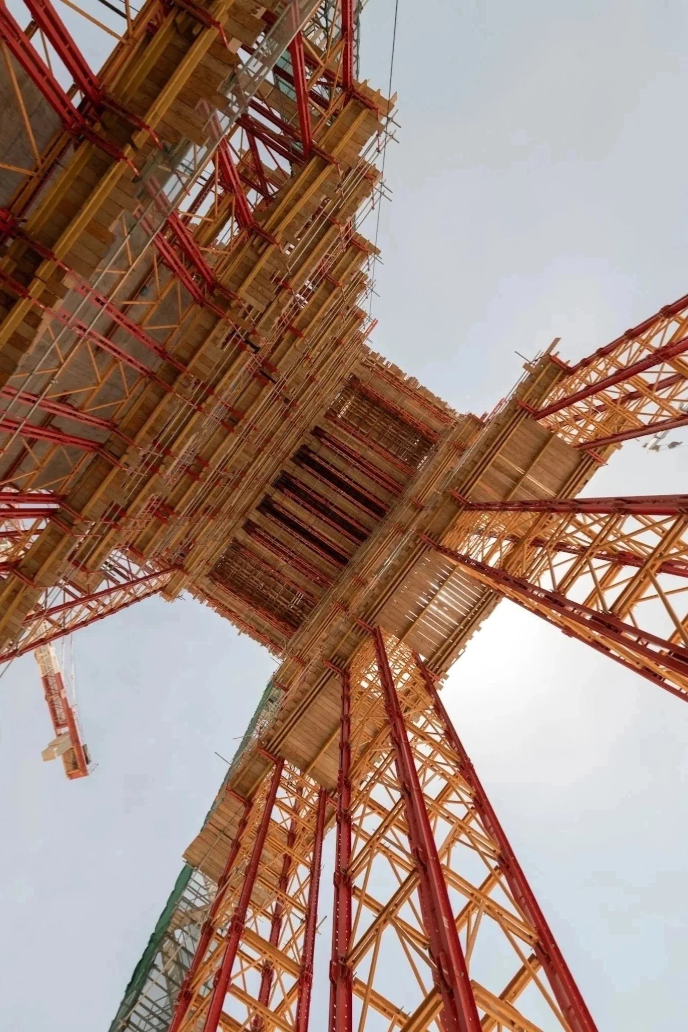 Looking up at a construction crane with a framework of metal beams and scaffolding, partially obscured by the sky.