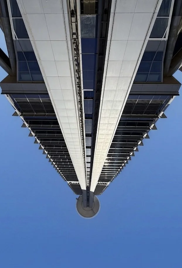 Looking up at a tall modern skyscraper with glass windows against a clear blue sky.