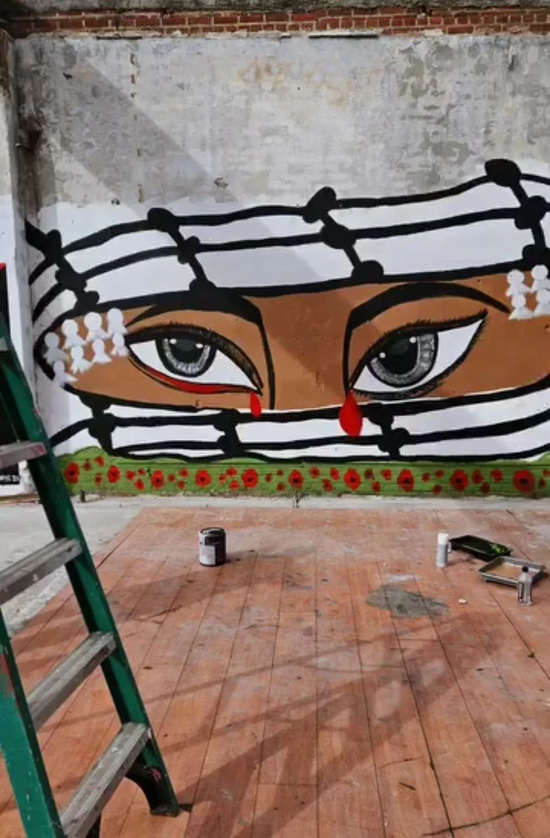 Street art mural depicting a face with large eyes and tear drops, surrounded by black and white striped pattern. Red poppies at the bottom and white flowers on the sides.