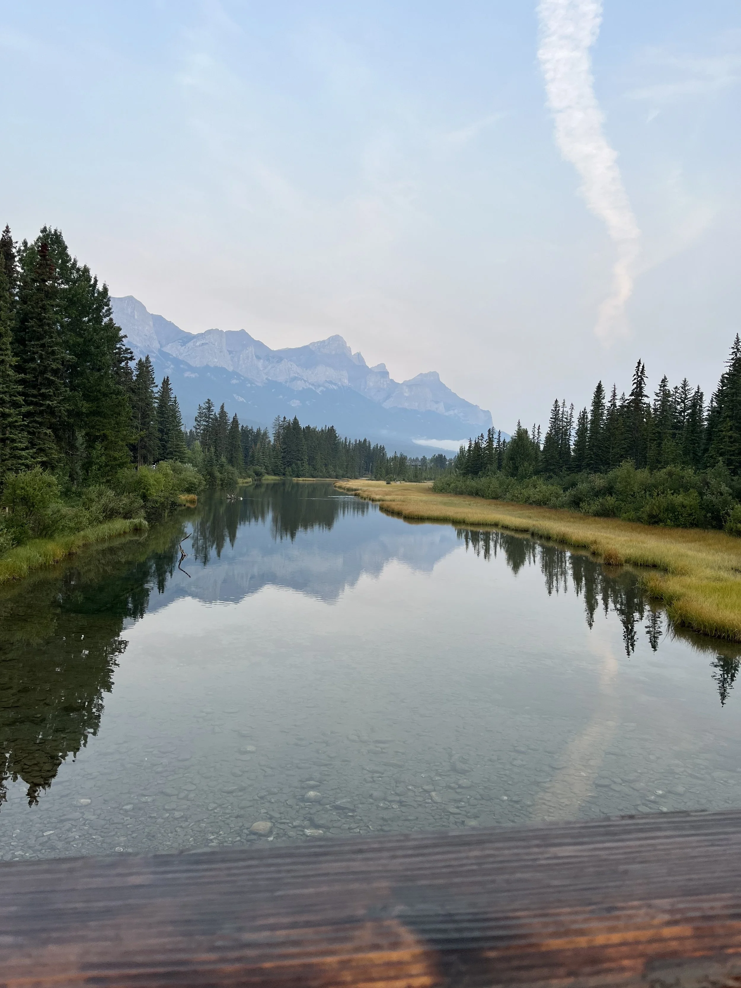 Mountain lake with evergreen trees along the shoreline and a mountain range in the background, reflected in the still water.