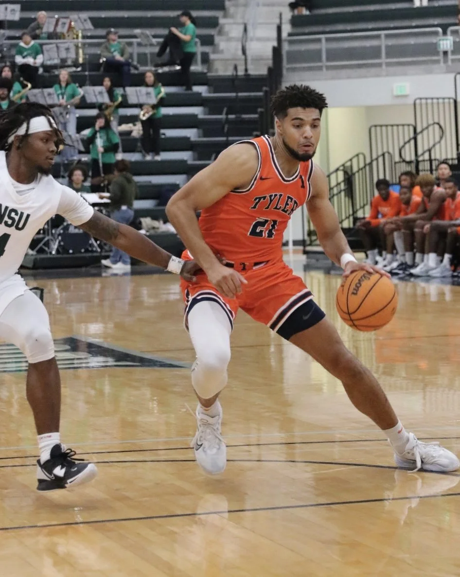 Two basketball players competing for the ball during a game in an indoor gym, with spectators and a band in the background.