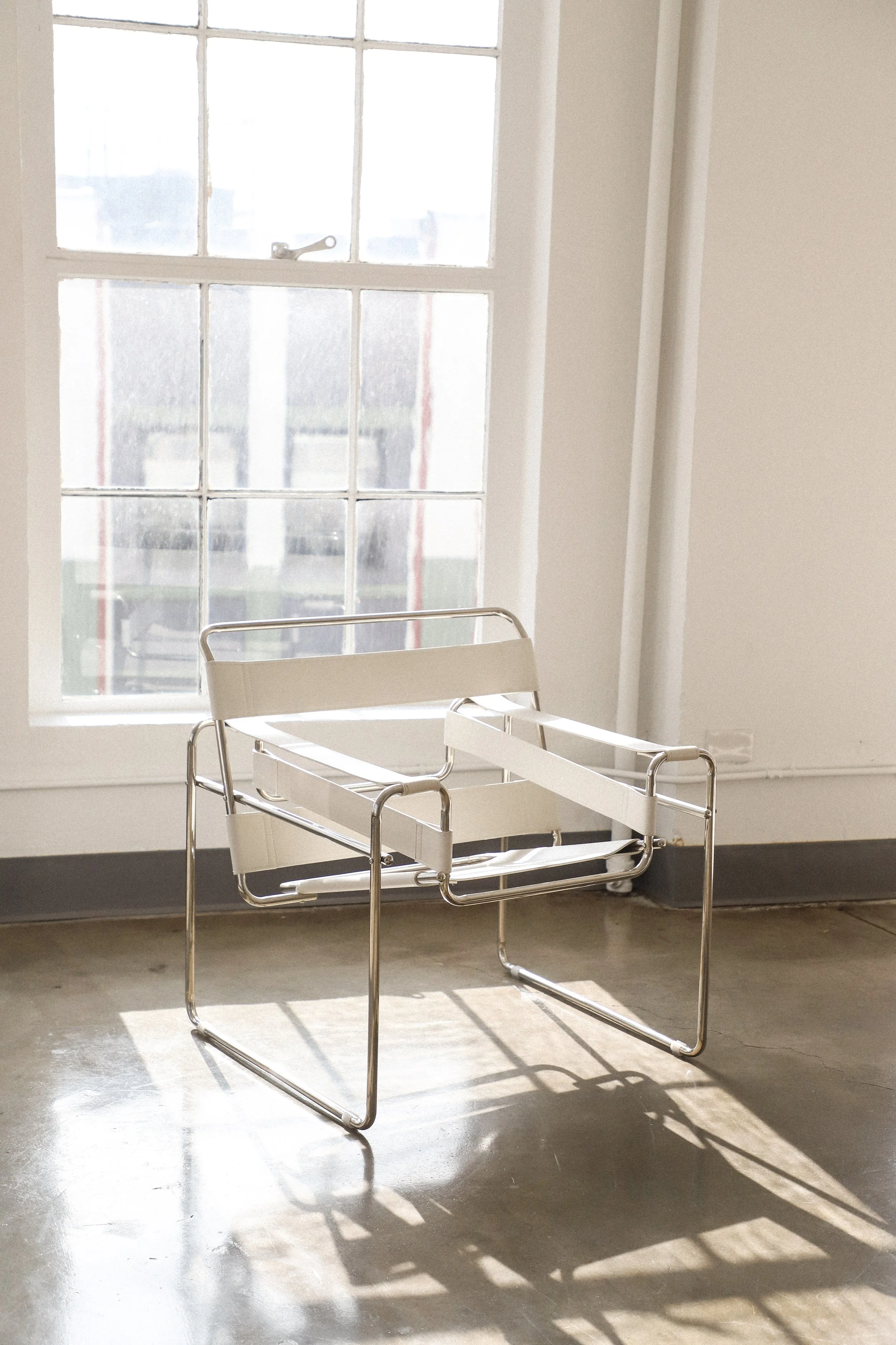 Empty hospital gurney with white vinyl padding and metal frame in a bright room with a large window, sunlight casting shadows on the floor.