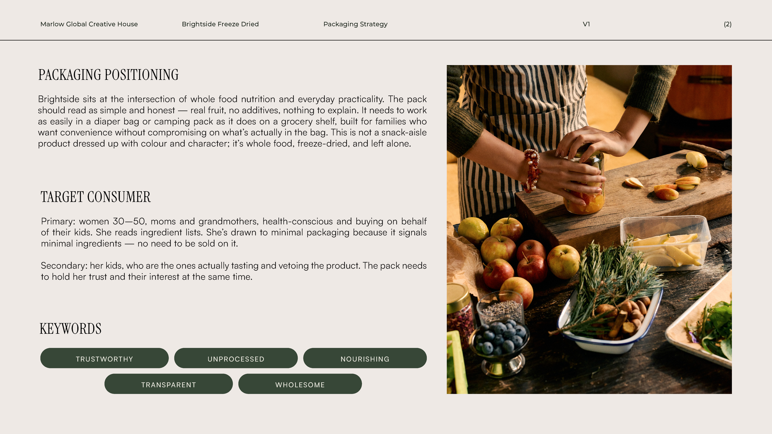 A person wearing a striped apron and a bracelet is preparing fruit in a rustic kitchen. There are apples, herbs, and cheese on the wooden counter, with a knife and other ingredients around.