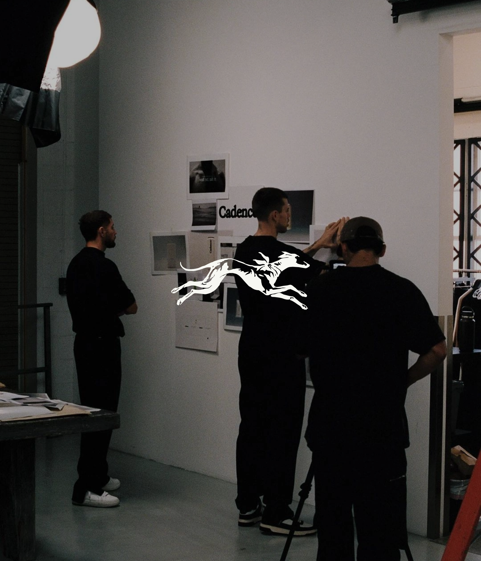 People standing in a room, some engaged in conversation, with photos and posters on the wall, and a large dragon logo in the foreground.