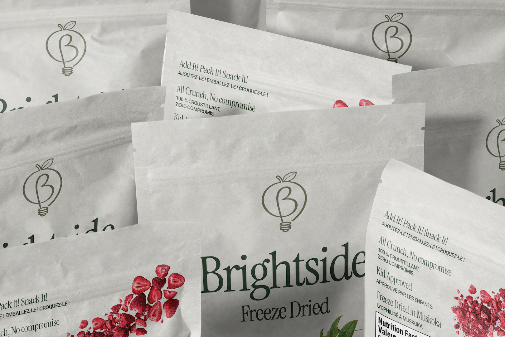 Several white snack packages with a logo of a lightbulb and a leaf, and the word 'Brightside' on the front. One package features a cluster of dried strawberries, and another shows dried raspberries, with product descriptions like 'Freeze Dried' and 'No compromise'.