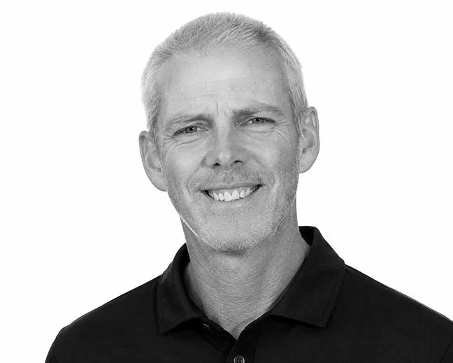 Black and white portrait of a smiling man with short gray hair, wearing a dark collared shirt.