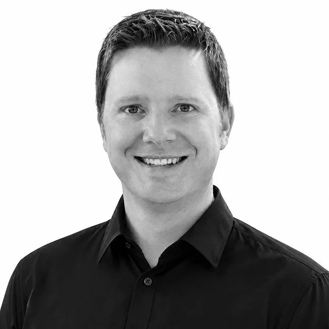 Black and white headshot of a smiling young man with short hair wearing a dark collared shirt.