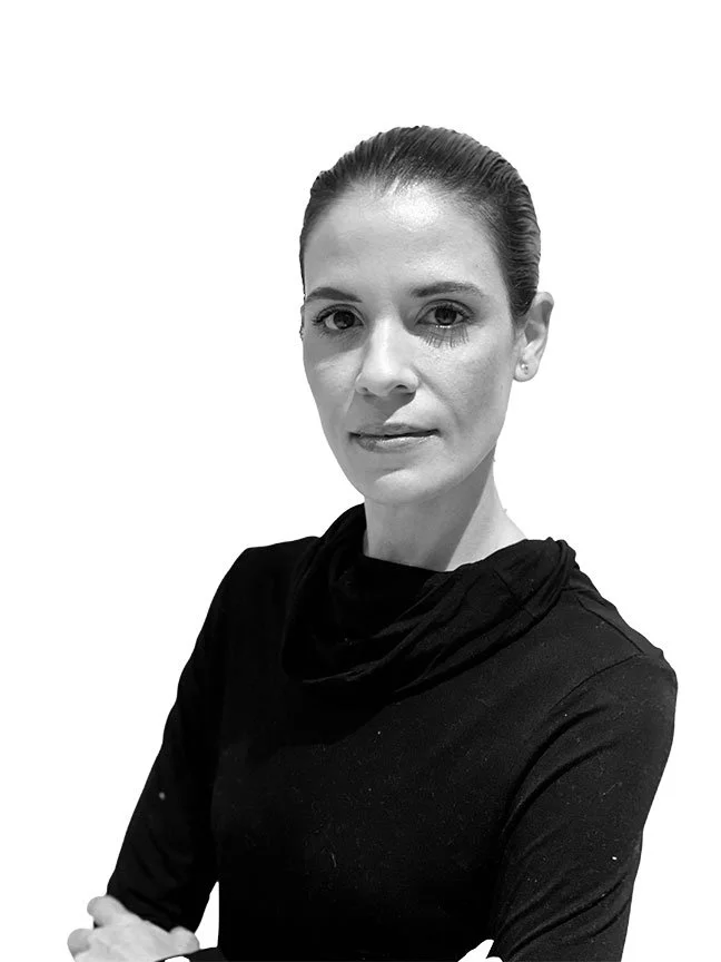 Black and white portrait of a woman with her hair pulled back, wearing a black top, against a plain white background.