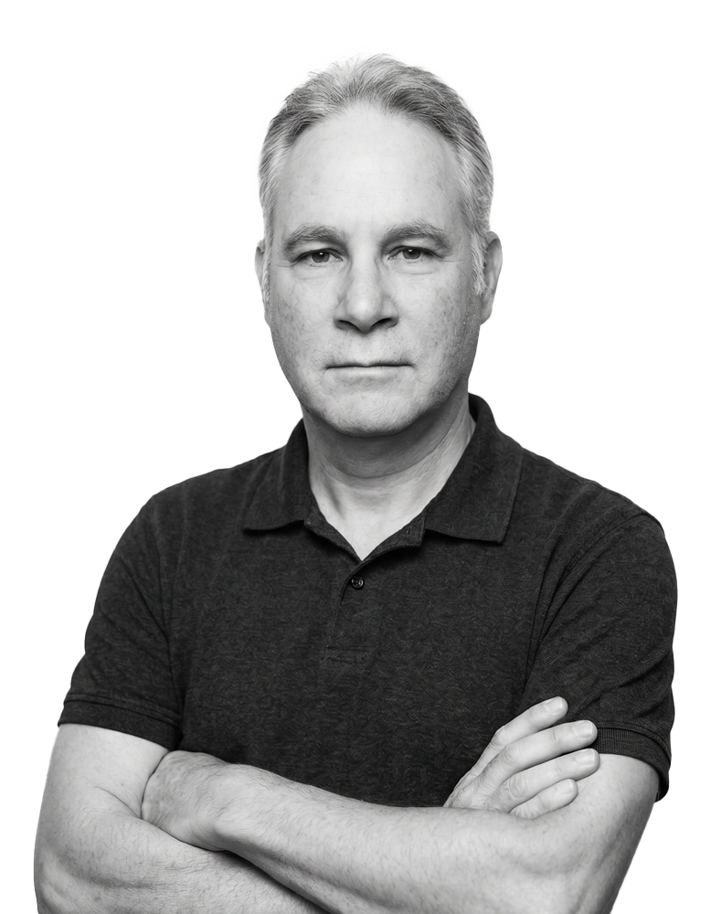 Black and white portrait of a middle-aged man with short, light-colored hair, wearing a dark polo shirt, crossing his arms, looking directly at the camera.