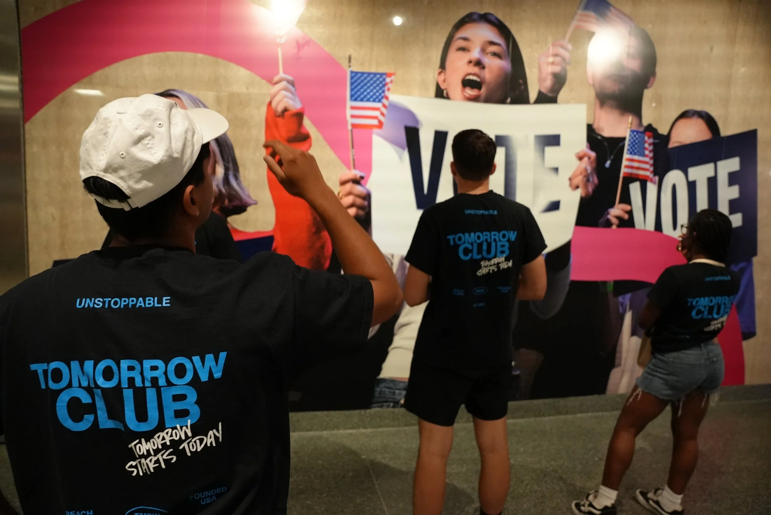 Group of people protesting with flags and a large sign that reads 'VOTE' during a political rally.