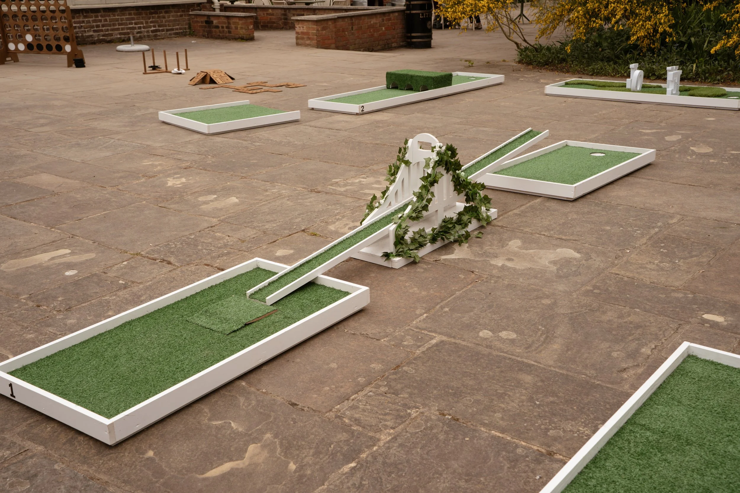 Miniature golf putting course with various obstacles and green turf sections on a paved outdoor area.