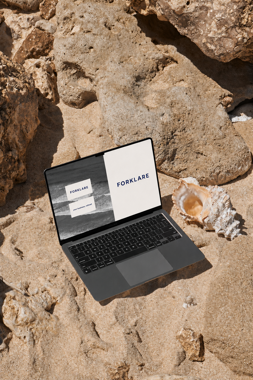 A laptop on sand among rocks and shells at the beach, displaying the logo and text for 'FORKLARE'.