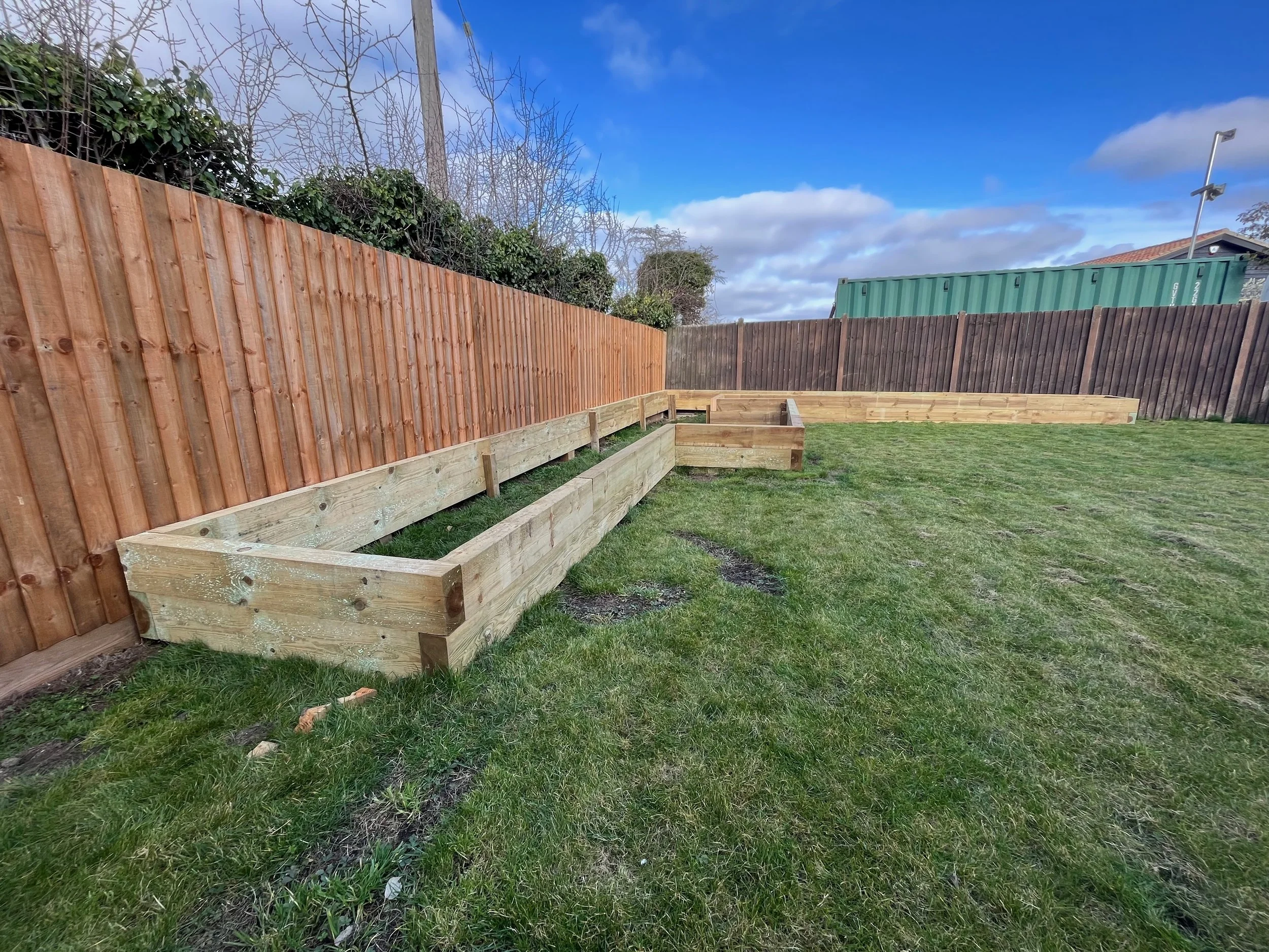 Backyard with new wooden fence, green grass, and cloudy blue sky.