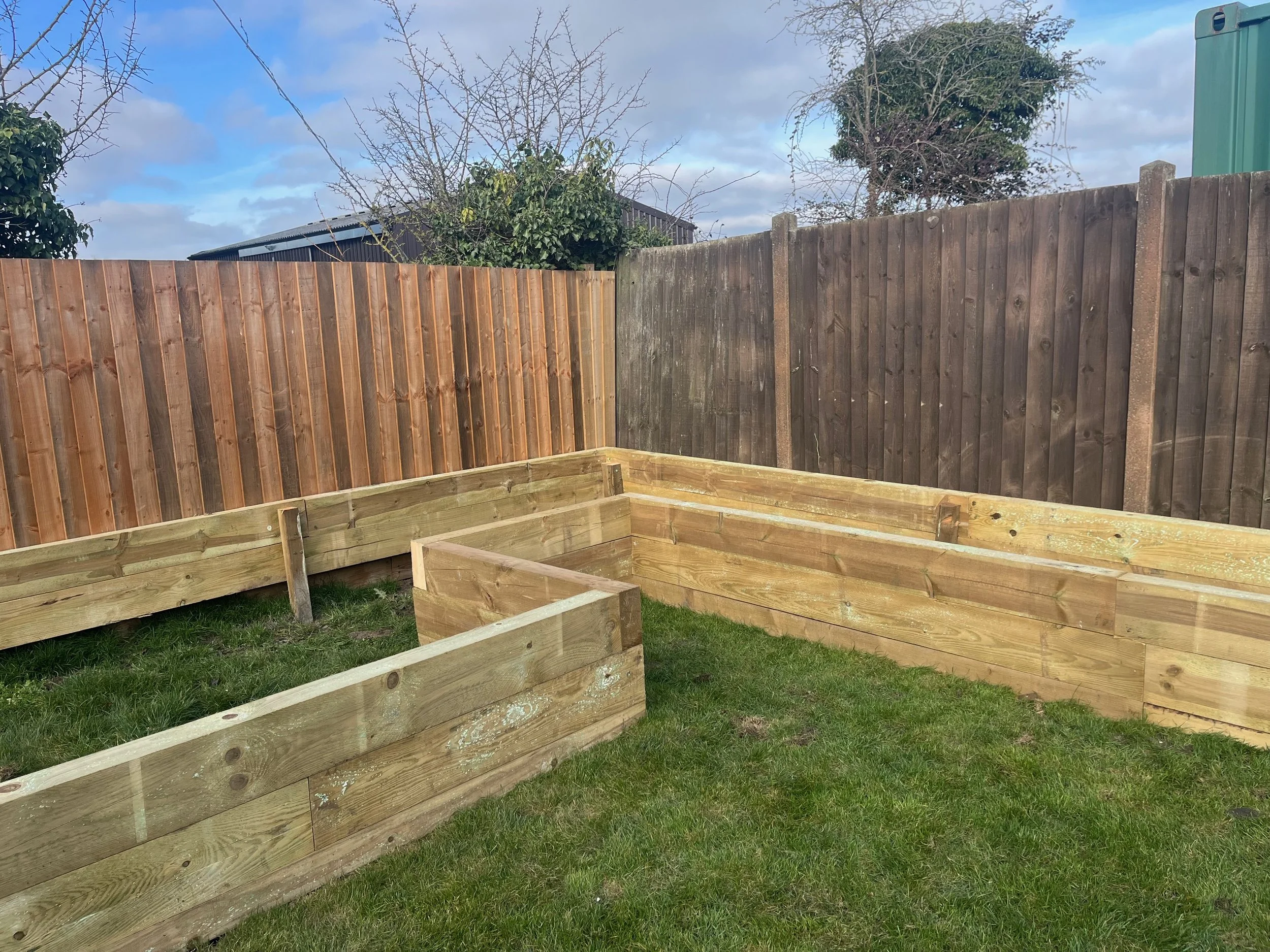A yard with a wooden fence, some green grass, and a partly cloudy sky with some clouds and patches of blue.