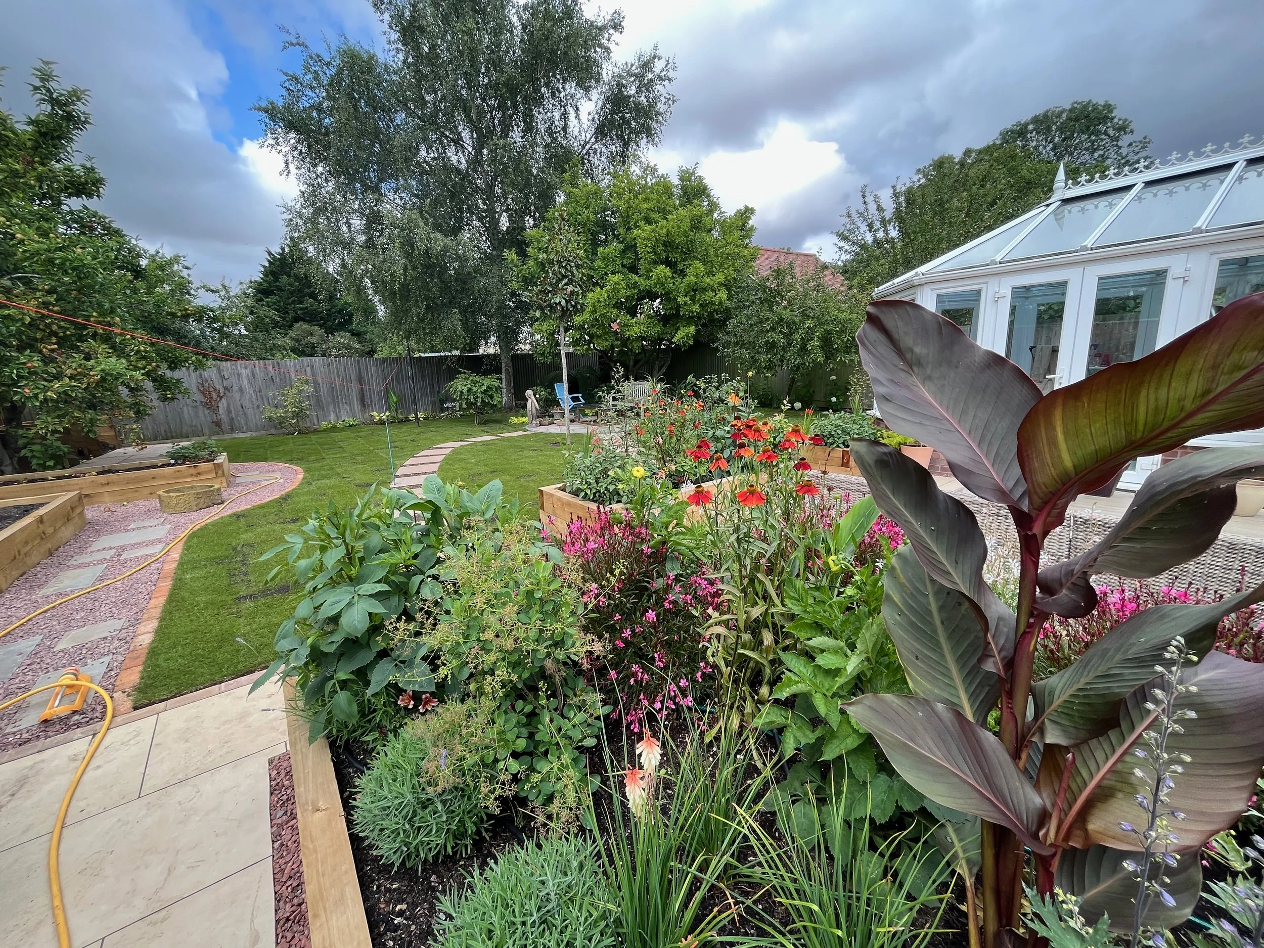 A back garden some months after landscaping and planting was completed for garden design Cambridge with various flowering plants, a stone pathway, trees.