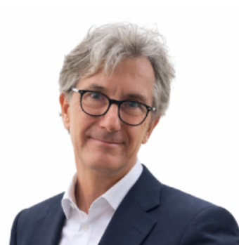 Ein Mann mit grauem Haar, Brille und Anzug, lächelnd, vor weißem Hintergrund.